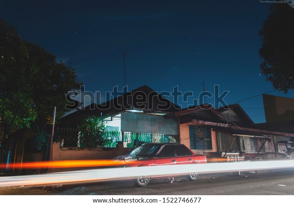 CAVITE, PHILIPPINES\
 – FEBRUARY 25 2019:  Long exposure shot of simple Bungalow\
concrete house in a subdivision in an Urban area in the Philippines\
with a cat under the\
car.