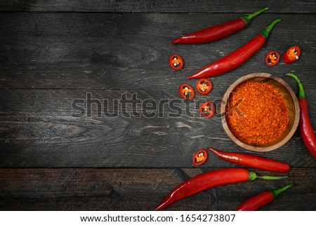 Cayenne in small bowl with chili on wooden table.