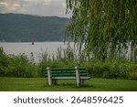 Cayuga Lake Inlet Beacon rises from the water beyond a serene bench and willow tree lake edge in Stewart Park, Ithaca, New York, USA