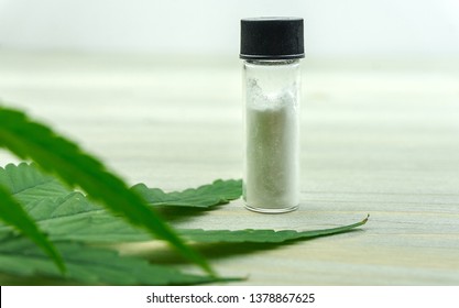 CBD Cannabidiol crystals isolate in glass container with Cannabis leaf on table