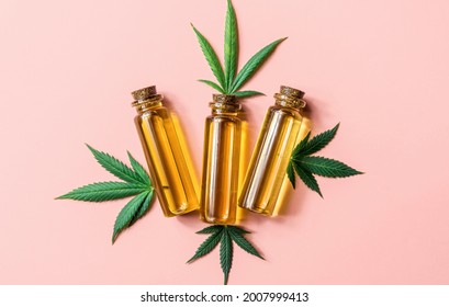 CBD Cannabidiol oil bottle and Cannabis leafs on pink background