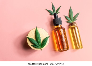 CBD Cannabidiol oil bottles Hemp skin care cream and Cannabis leafs on pink background