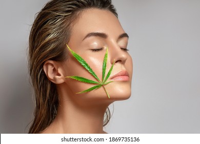 CBD Cosmetics Concept. Beautiful Woman With A Cannabis Leaf On Gray Background