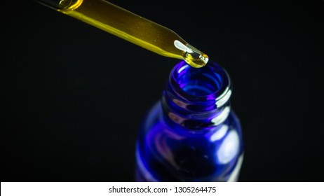 CBD Extract Tincture Liquid Dripping Into Blue Bottle Isolated On Black