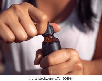 CBD Oil In Brown Bottle, Close Up. Woman Using CBD Oil.