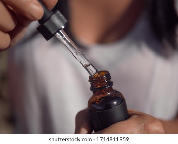 CBD Oil In Eye Dropper And Brown Bottle, Close Up. Woman Using CBD Oil.