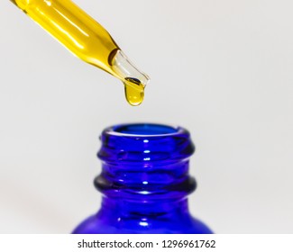 CBD oil tincture dropping into blue bottle up close isolated on white background