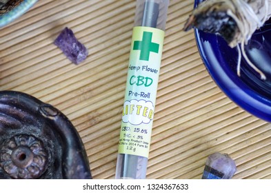 CBD Pre-Rolled Blunt, Hemp Flower, Unlit In Tube On Bamboo Mat, Surrounded By Healing Stones, Sage, Pendants 