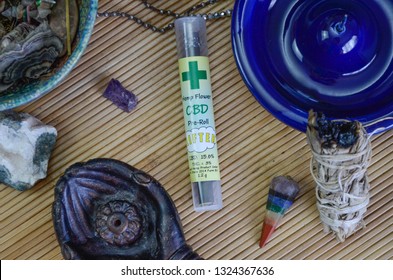 CBD Pre-Rolled Blunt, Hemp Flower, Unlit In Tube On Bamboo Mat, Surrounded By Healing Stones, Sage, Pendants 