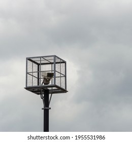 A CCTV camera inside a security cage on the top of a pole.