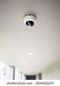 CCTV camera on white ceiling at walkway on ground floors in apartment building with copy space, vertical style.
