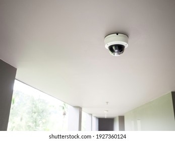 CCTV camera on white ceiling at walkway on ground floors in apartment building with copy space.
