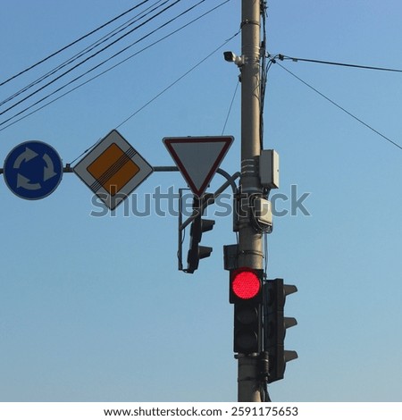 CCTV camera, traffic lights and priority signs for cars at a roundabout. Traffic signs and video surveillance of a busy intersection
