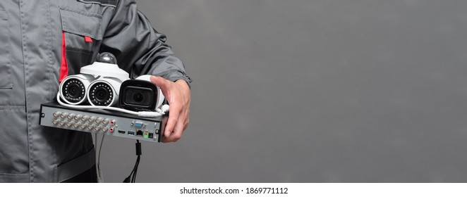 CCTV camera and video surveillance equipment in the worker hands on the gray background with copy space.
