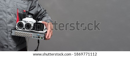 CCTV camera and video surveillance equipment in the worker hands on the gray background with copy space.