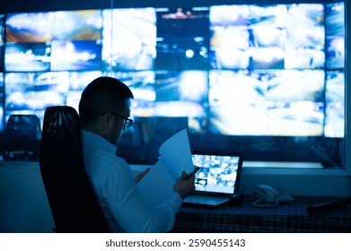 CCTV officer sitting and checking reports on clipboard. with the background of multiple monitors - Powered by Shutterstock - Get 15% off with code: PIKWIZARD15
