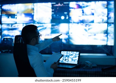 CCTV officer sitting and checking reports on clipboard. along with pointing at multiple monitors - Powered by Shutterstock - Get 15% off with code: PIKWIZARD15