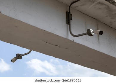 CCTV security camera mounted under a pedestrian bridge, monitoring both directions of a city street for safety and surveillance purposes.