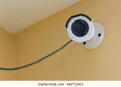 The CCTV Security Camera Operating On Orange Cement Wall Inside Room.