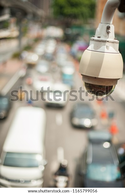CCTV, surveillance security video camera\
hanging on top the road monitoring for security and safety purpose,\
heavy traffic in blurry\
background.