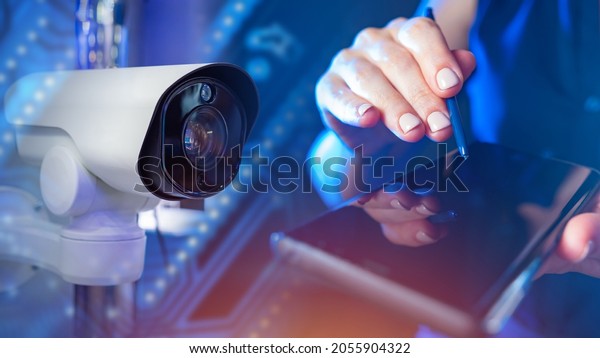 CCTV system application concept. CCTV camera next\
to woman\'s hands. Smartphone in hands of businesswoman close up.\
Remote video surveillance metaphor. Remote monitoring of video\
surveillance system
