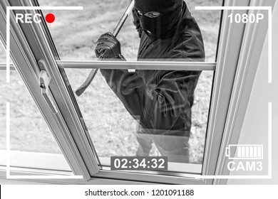 CCTV view of burglar breaking in to home through window with crowbar - Shutterstock ID 1201091188