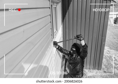 CCTV view of burglar breaking in to home through window with crowbar. Protection of a private residential building with the help of an external video surveillance system. black and white style