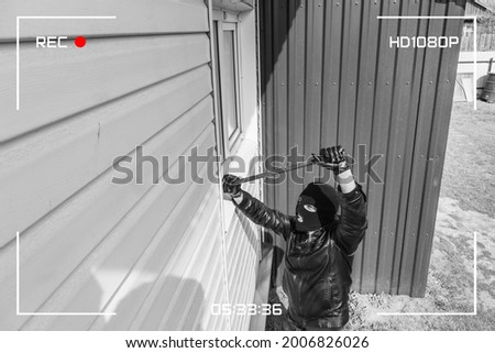 CCTV view of burglar breaking in to home through window with crowbar. Protection of a private residential building with the help of an external video surveillance system. black and white style