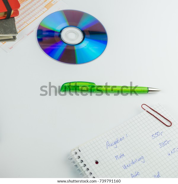 CD\
and green ballpoint pen, next to it a writing pad with pen, on it\
the German words for expenses, rent, insurance and\
car
