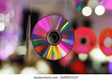 CD hanging on thread with rainbow surface and multicolored bokeh lights behind. Captures a retro and vibrant party mood.