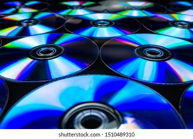 CDs lying on a black background with colorful reflections of light.