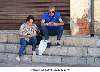 Cefalu, Italy - October 23, 2022: Elderly Tourist Couple Sitting In The Shade On A Stone Staircase