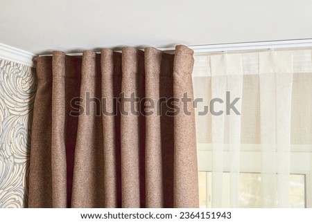 Ceiling cornice with drapes white curtain or tulle. Interior details close up. White ceiling, plastic ceiling cornice with two rails brown matting fabric curtains and transparent curtains near window.