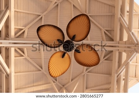 A ceiling fan with leaf-shaped blades mounted on a white wooden vaulted ceiling structure.