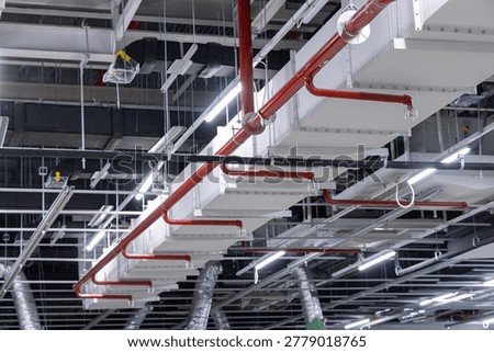 Ceiling infrastructure inside an industrial building showing red fire sprinkler pipes, ventilation ducts, lighting, and cable trays during installation.