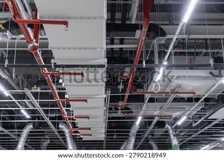 Ceiling infrastructure inside an industrial building showing red fire sprinkler pipes, ventilation ducts, lighting, and cable trays during installation.