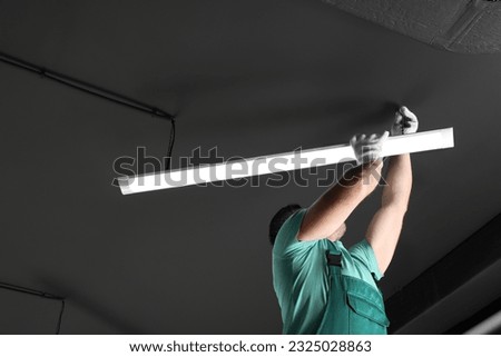 Ceiling light. Electrician installing led linear lamp indoors. Space for text