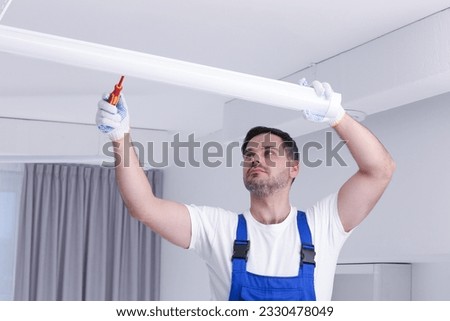 Ceiling light. Electrician installing led linear lamp indoors