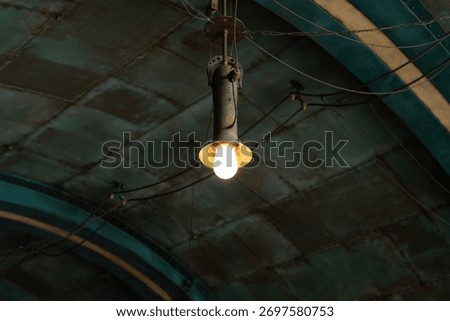 A ceiling lighting bulb that glowing in warmlight shade, it hanging from the ceiling in mine tunnel or industial workplace. Object with selective focus.