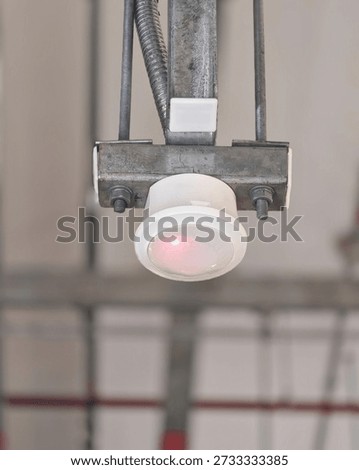 Ceiling mounted motion sensor detector installed on metal conduit, used for lighting control, security and energy efficiency in commercial building interior