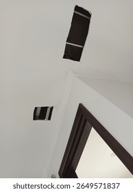 Ceiling with two rectangular cutouts for maintenance or installation, exposing pipes and wiring above, near a wooden door frame in an interior space