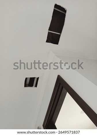 Ceiling with two rectangular cutouts for maintenance or installation, exposing pipes and wiring above, near a wooden door frame in an interior space