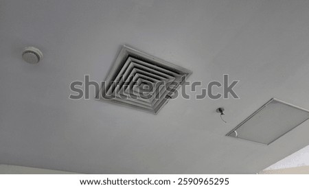 Ceiling view featuring an air vent, light fixture, and access panel, capturing a common building interior element.