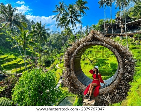 Ceking Rice Terrace (Tegalalang Rice Terrace), Ubud, Bali, Indonesia, October 2023. A stylish girl in a red dress, and a straw hat sitting on the spot view overlooking the tropical paradise