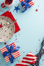 Celebrate Fourth Of July With This Patriotic Table Arrangement. Vertical Top View, Featuring Plate, Cup, Cutlery, Napkin, Confetti, Tie, Gift Boxes On Light Blue Background. Space For Your Text Or Ad