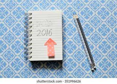 Celebrating 2016. A notepad  with a post-it and a pen with handwritten year 2016  in a blue graphic background