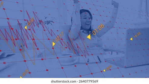 Celebrating Asian woman raising arms at office desk, with silver laptop and financial data overlay. Achievement, success, technology, business, innovation, optimism, workspace