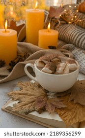 Celebrating autumn holidays at cozy home with cup hot chocolate marshmallows cacao on the windowsill Hygge atmosphere Thanksgiving candle on cozy knitted sweater in warm yellow lights. Selective focus - Shutterstock ID 2189356299