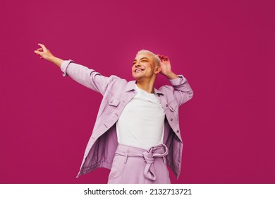 Celebrating the beauty of life. Happy queer man celebrating with his arms outstretched in a studio. Cheerful non-conforming man smiling while standing against a purple background.