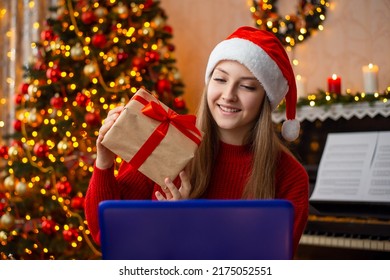 Celebrating Christmas With Close People Online. Smiling Girl Showing Present To The Web Cam Of The Laptop, Having Conversation With A Person Via Internet